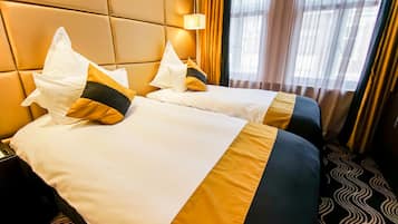 Une chambre d’hôtel avec deux lits, une tête de lit, une table de chevet, une lampe et une fenêtre avec des rideaux.