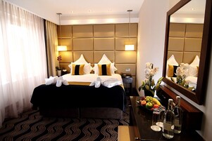 A hotel room with a large bed, a bedside table with a fruit bowl, a mirror, and a nightstand.