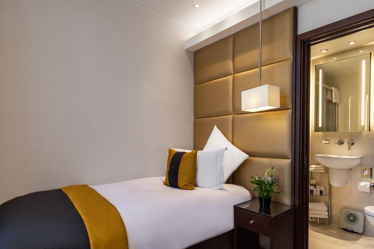 A hotel room with a bed, bedside table, and a bathroom visible through an open door.