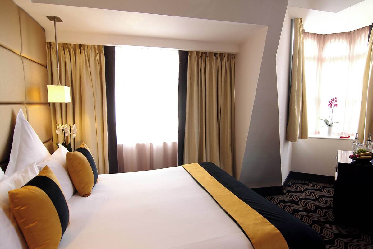 A hotel room with a large bed, a desk with a lamp, and a window with curtains.