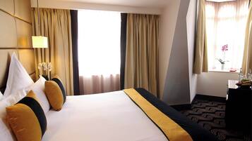 A hotel room with a large bed, a desk with a lamp, and a window with curtains.