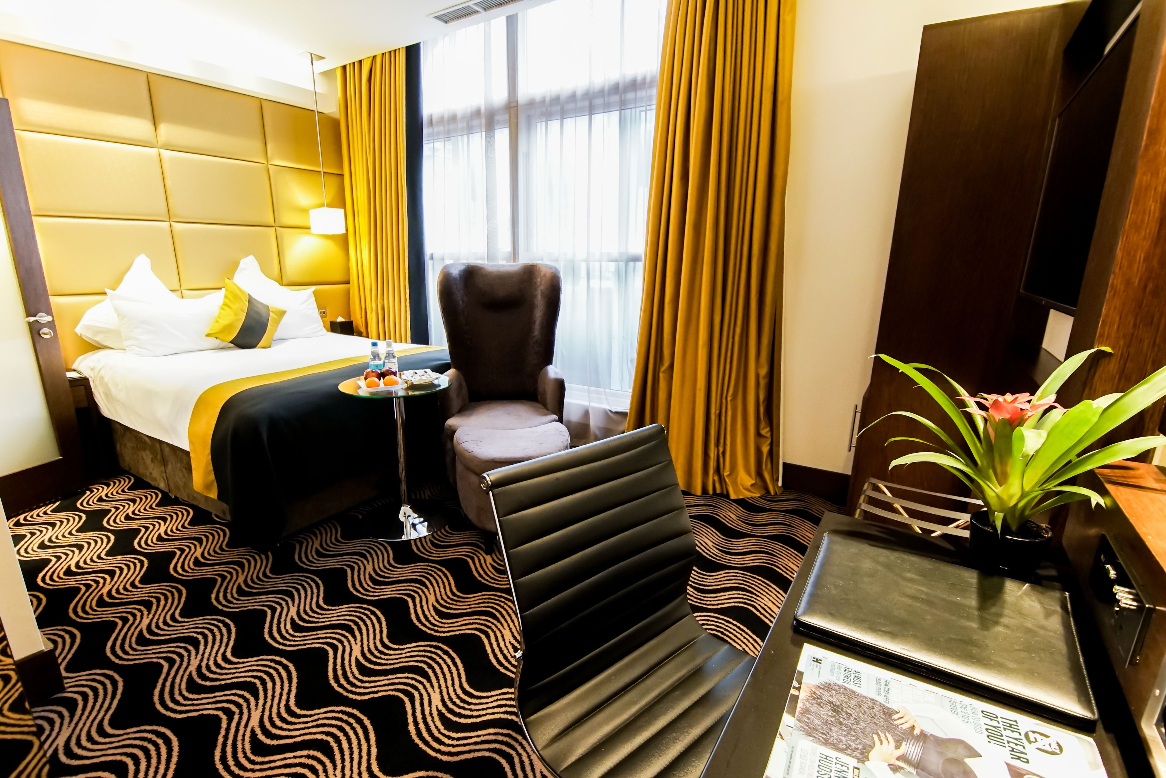 Habitación de hotel con una cama grande, una silla, una mesita, una planta en maceta y una ventana con cortinas.