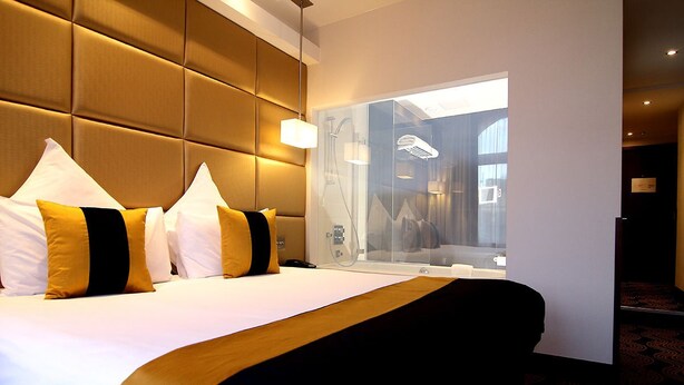 A hotel room with a large bed, a glass partition, and a view of a bathroom. - Montcalm Piccadilly Townhouse, London West End (London)