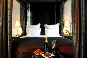 A luxurious hotel room with a large bed, two bedside lamps, a bottle of champagne, and a plate of strawberries.