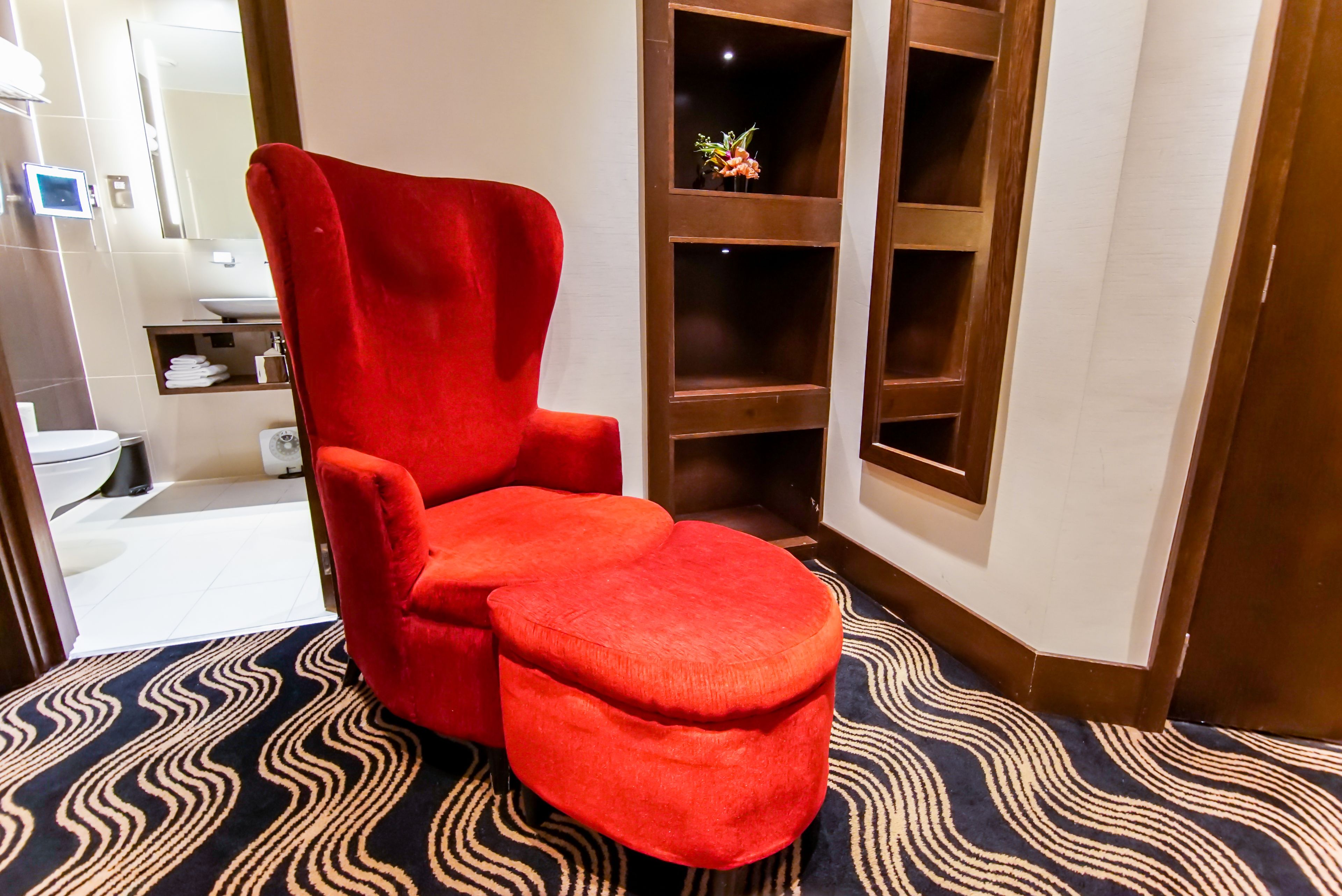 Un sillón rojo y un reposapiés en un rincón de una habitación con alfombra estampada.