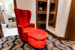 A red armchair and ottoman in a corner of a room with a patterned carpet.