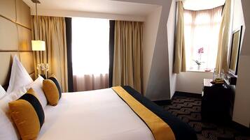 A hotel room with a large bed, a desk, and a window with curtains.