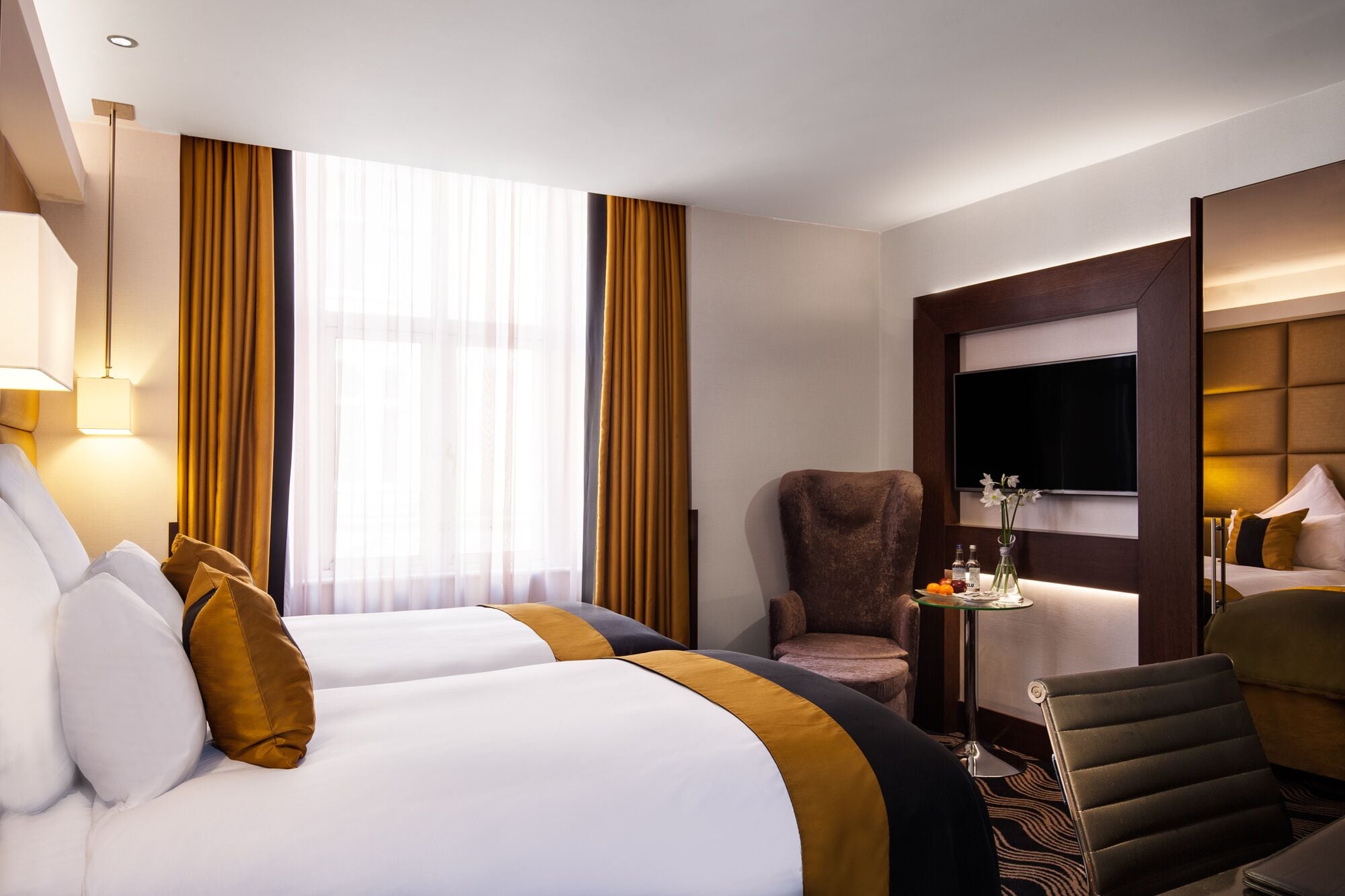Une chambre d’hôtel avec deux lits, une chaise, une petite table avec un vase et un téléviseur.