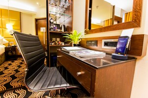 Ein Hotelzimmer mit modernem Schreibtisch, einem Sessel, einem Spiegel, einer Pflanze und einer Ladestation.