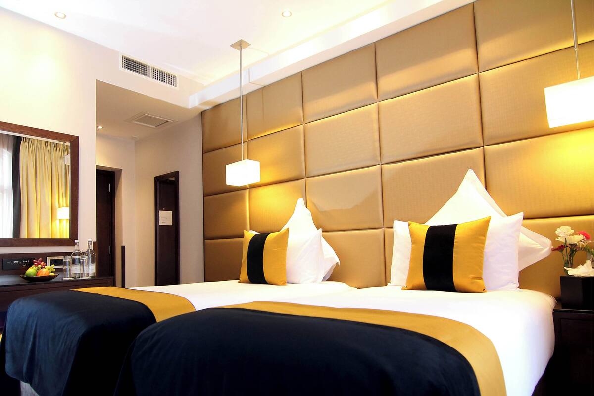A hotel room with a large bed, two bedside tables, a nightstand with a vase of flowers, and a mirror with curtains.