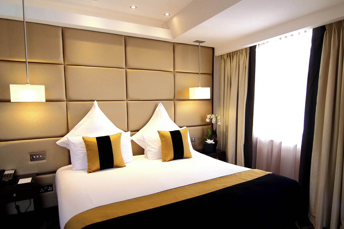 A hotel room with a large bed, two bedside lamps, a nightstand, and a potted plant.