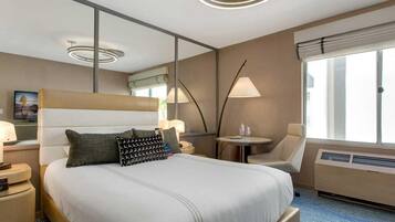 A hotel room with a large bed, bedside tables, a chair, a small table, a lamp, a window, and a ceiling light.