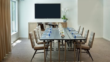 Een vergaderzaal met een lange tafel, stoelen, een flatscreen televisie en een potplant.