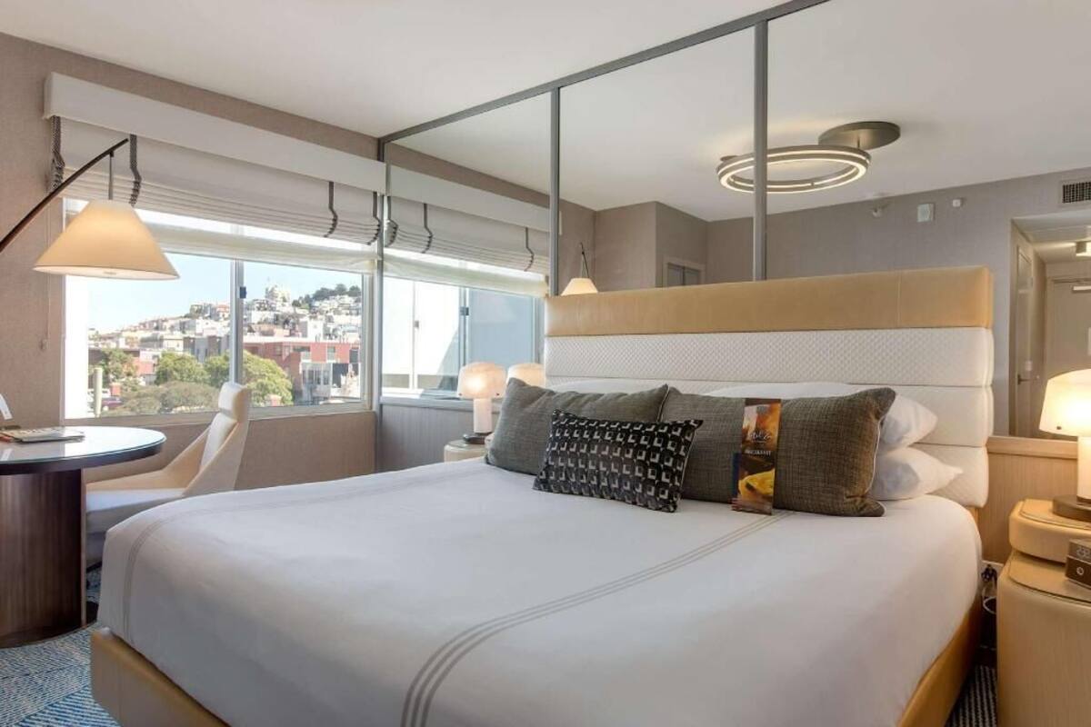A hotel room with a large bed, bedside tables, a desk, and a view of the city.