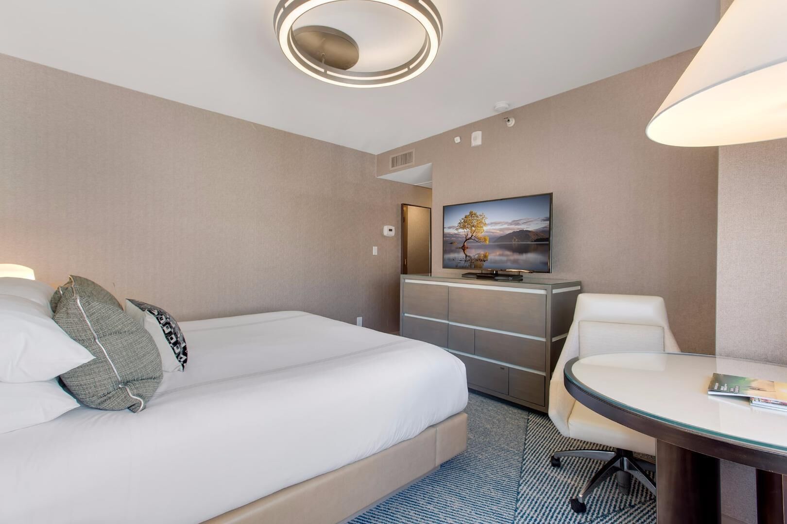 A hotel room with a bed, a desk, a chair, a television, and a wall-mounted artwork.