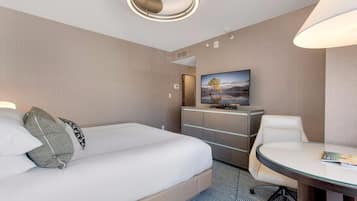 A hotel room with a bed, a desk, a chair, a television, and a wall-mounted artwork.