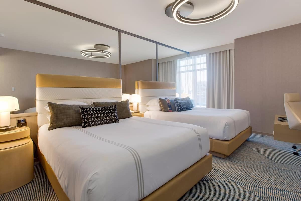 Une chambre d’hôtel avec deux lits, un grand miroir et un luminaire moderne au plafond.