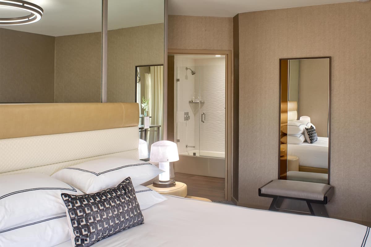 Une chambre d’hôtel avec un lit, une table de chevet, une lampe et un grand miroir.