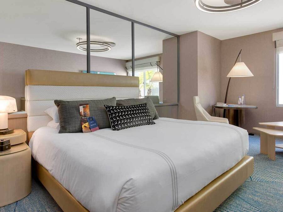 A hotel room with a large bed, bedside tables, a desk, and a lamp.
