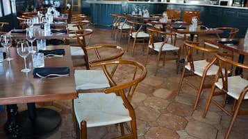 Un restaurante con mesas y sillas de madera, suelo de baldosas y una cocina al fondo.