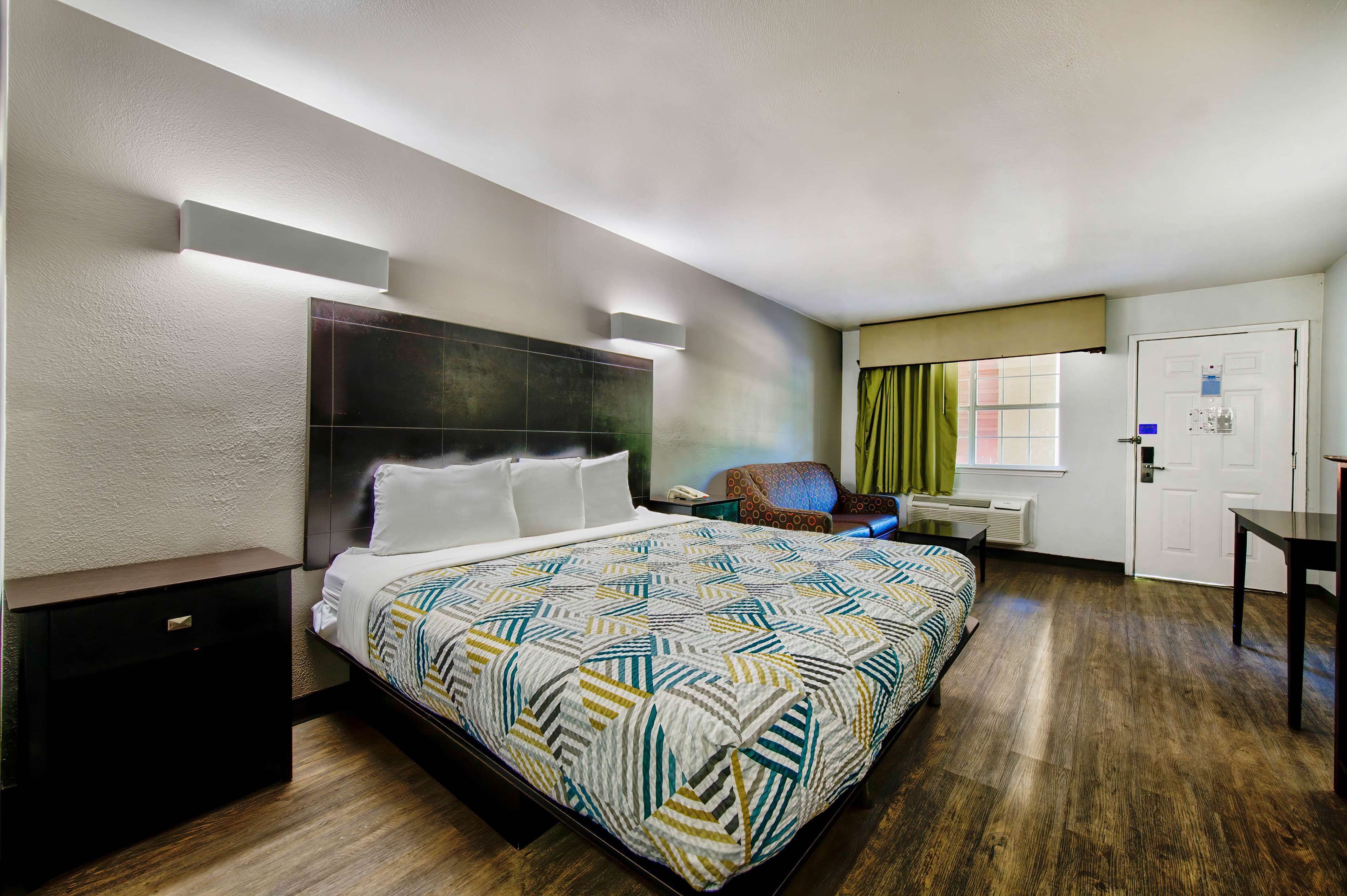 Una habitación de hotel con una cama grande, una mesita de noche, una silla, un escritorio y una puerta.
