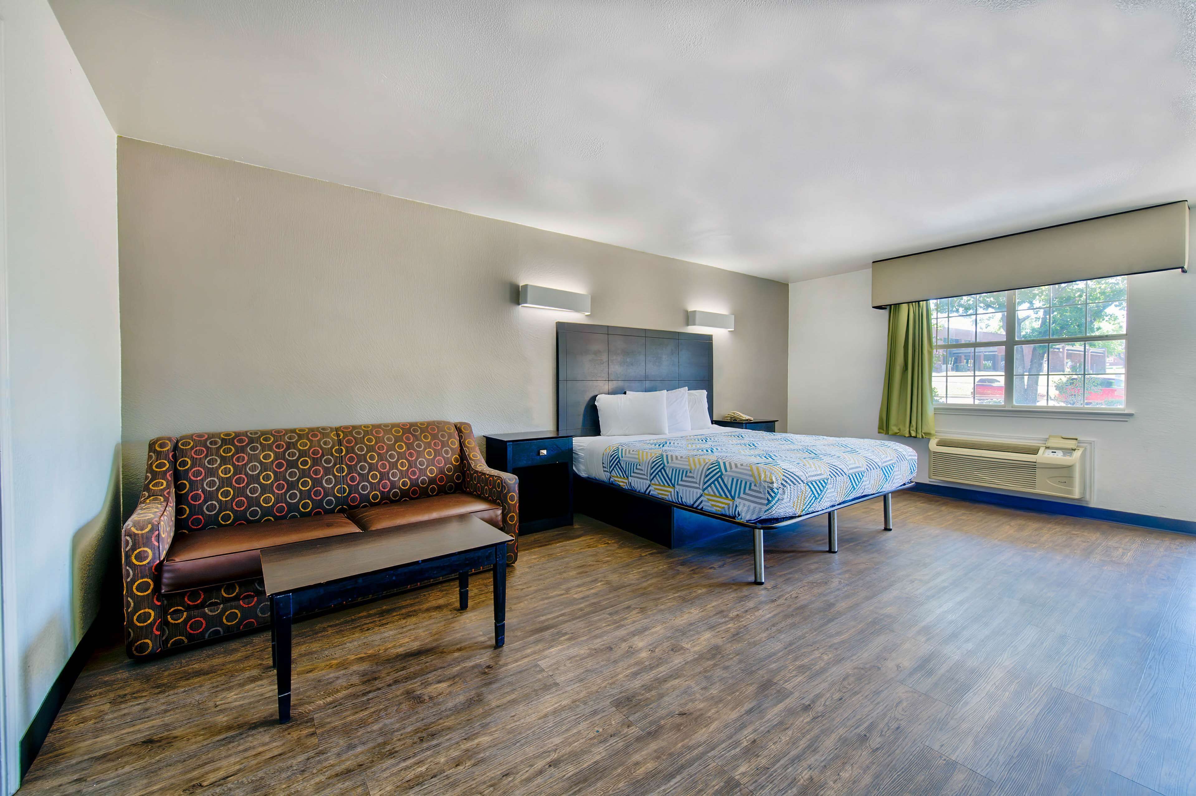 A hotel room with a bed, a sofa, a nightstand, and a window with curtains.