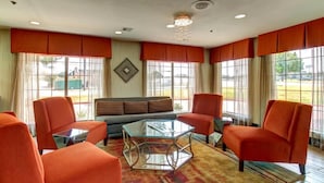 Un salon avec des fauteuils orange, une table basse en verre et un canapé.
