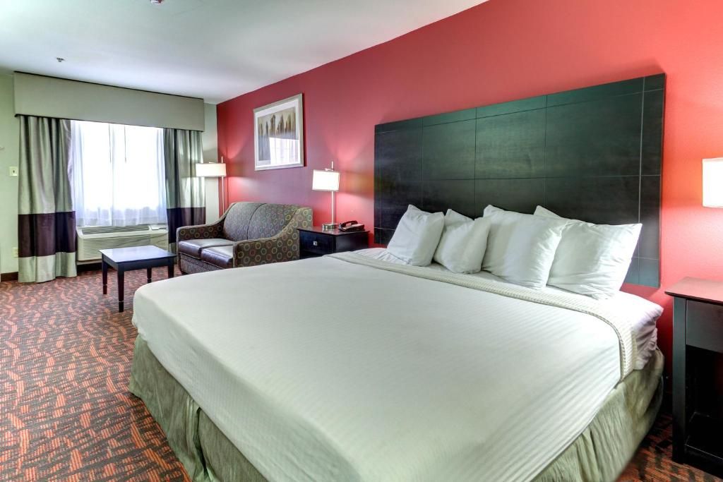 A hotel room with a large bed, a chair, a desk, and a window with curtains.