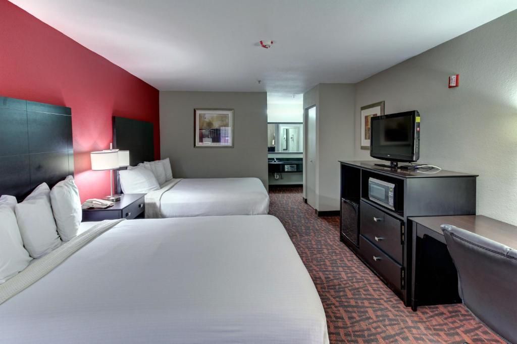 A hotel room with two beds, a desk with a computer, a television, and a kitchenette in the background.