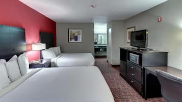 A hotel room with two beds, a desk with a computer, a television, and a kitchenette in the background.