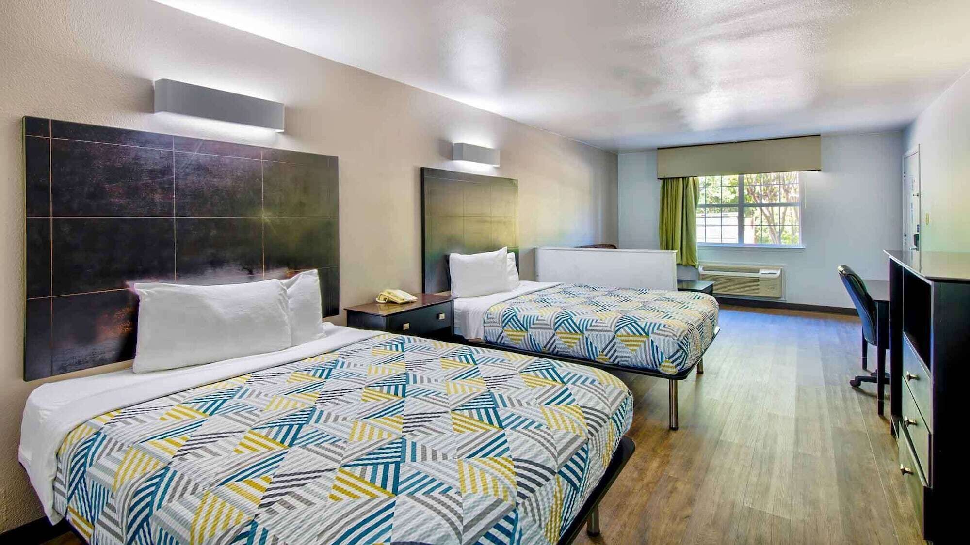 Habitación de hotel con dos camas, un escritorio y una ventana con cortinas.