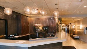 Un área de recepción moderna con un mostrador de madera, lámparas colgantes de vidrio y un largo pasillo con asientos.