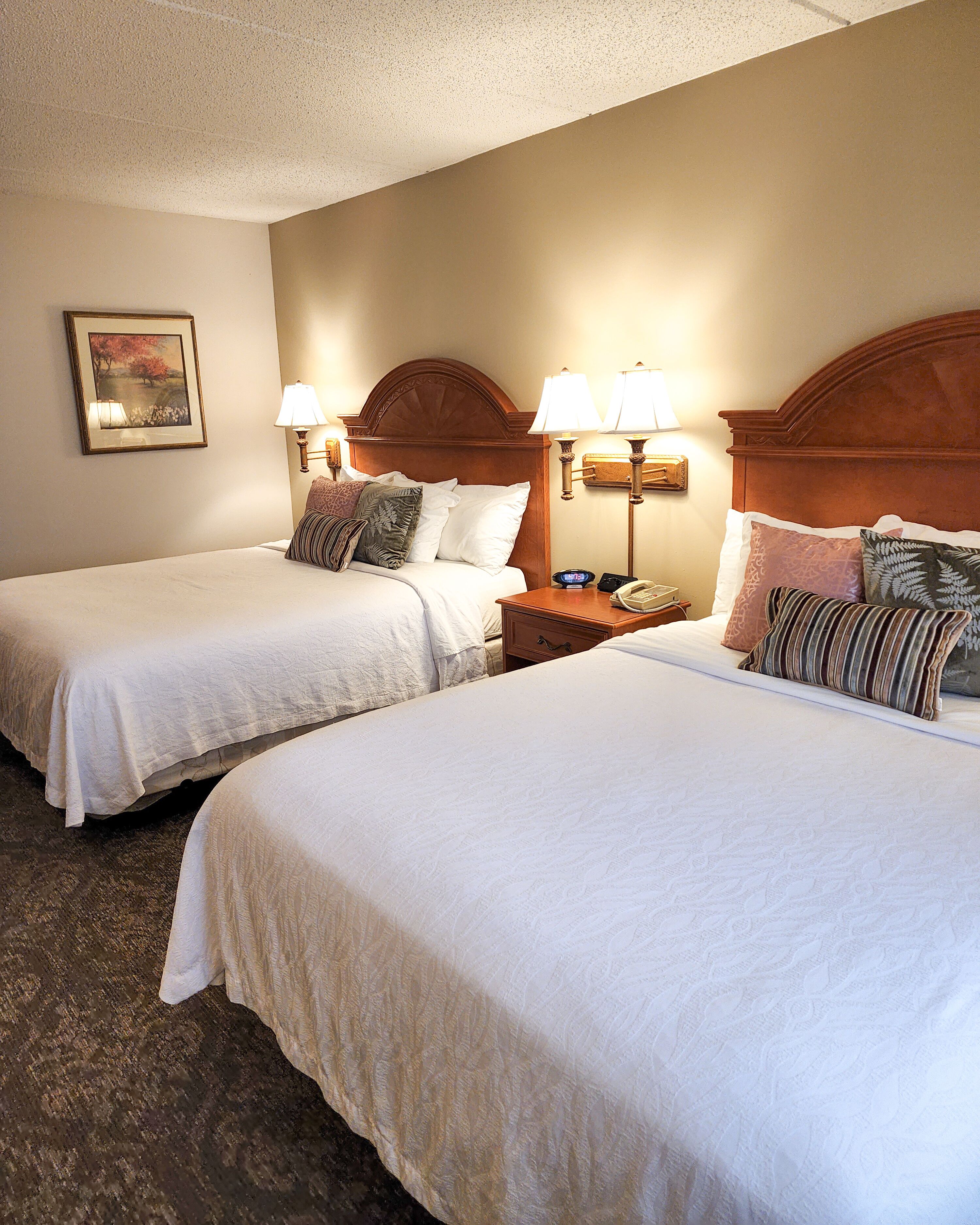 A hotel room with two single beds, each with a nightstand, bedside lamps, and a framed picture on the wall.