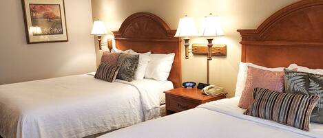 A hotel room with two single beds, each with a nightstand, bedside lamps, and a framed picture on the wall.
