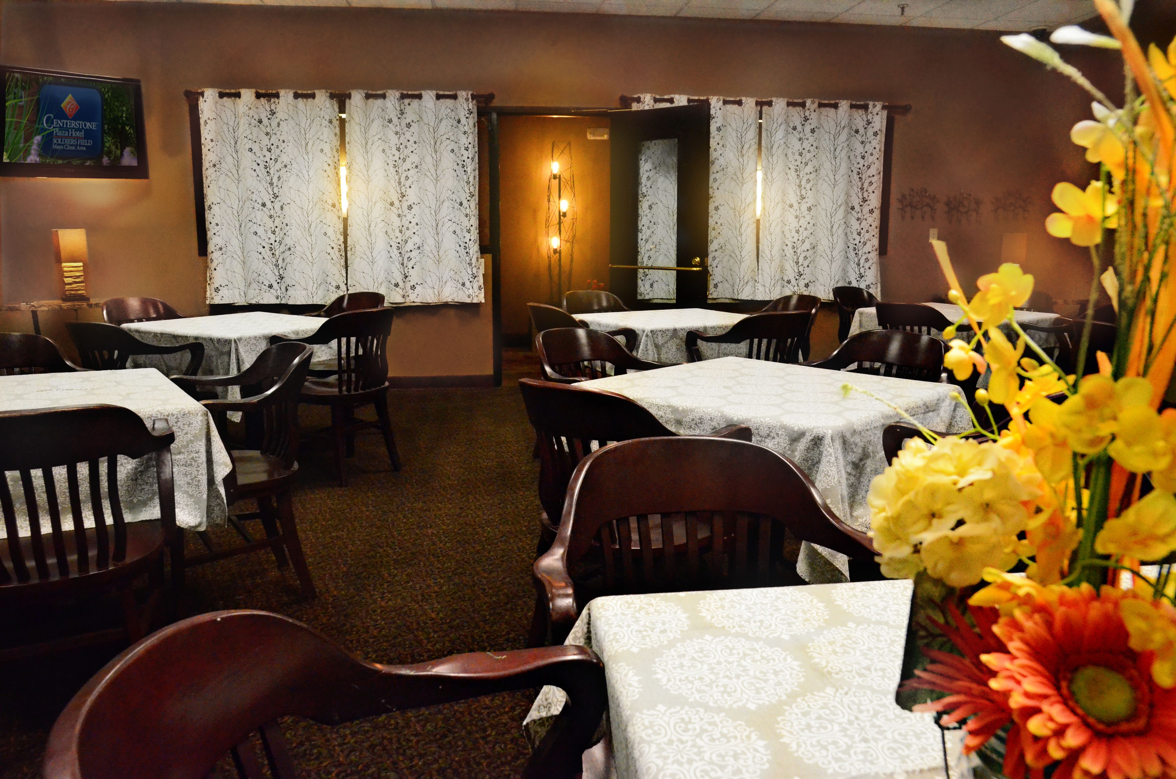 A dining area with tables and chairs, floral decorations, and a mirror on the wall.