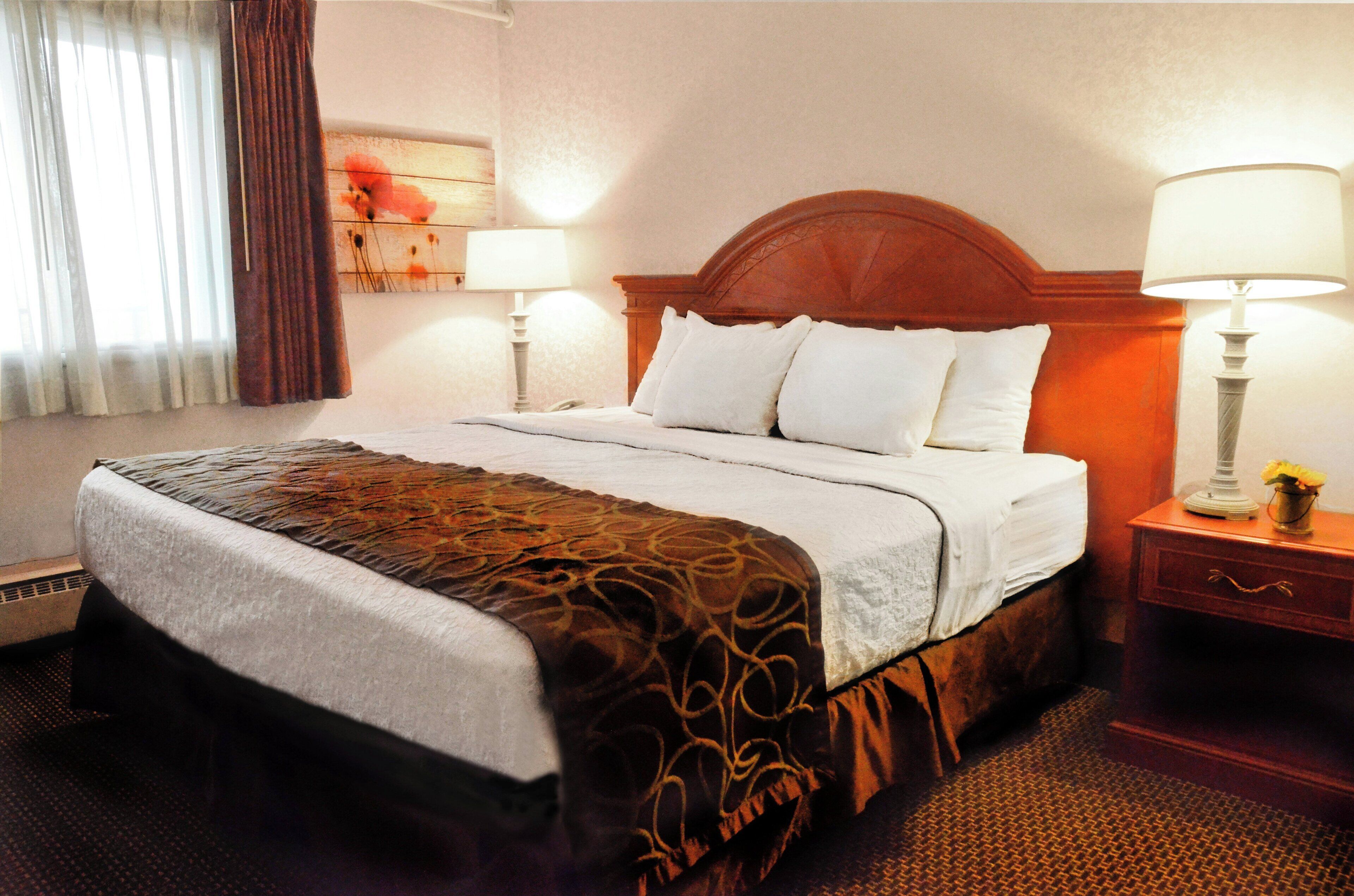 A hotel room with a large bed, two bedside lamps, a nightstand with a vase, and a painting on the wall.