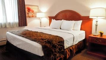 A hotel room with a large bed, two bedside lamps, a nightstand with a vase, and a painting on the wall.