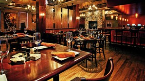 Interior de restaurante con mesas y sillas de madera, y pared de piedra.