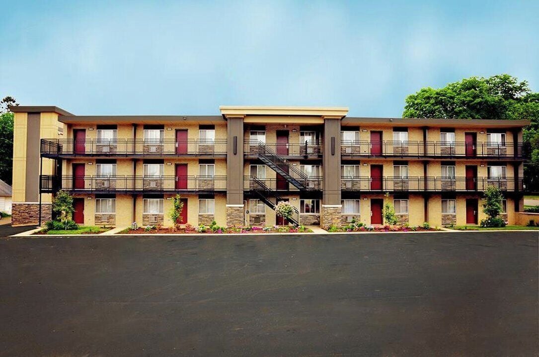 A multi-story motel with a central staircase, individual rooms with balconies, and a parking lot in front.