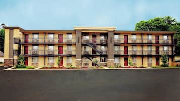 A multi-story motel with a central staircase, individual rooms with balconies, and a parking lot in front.