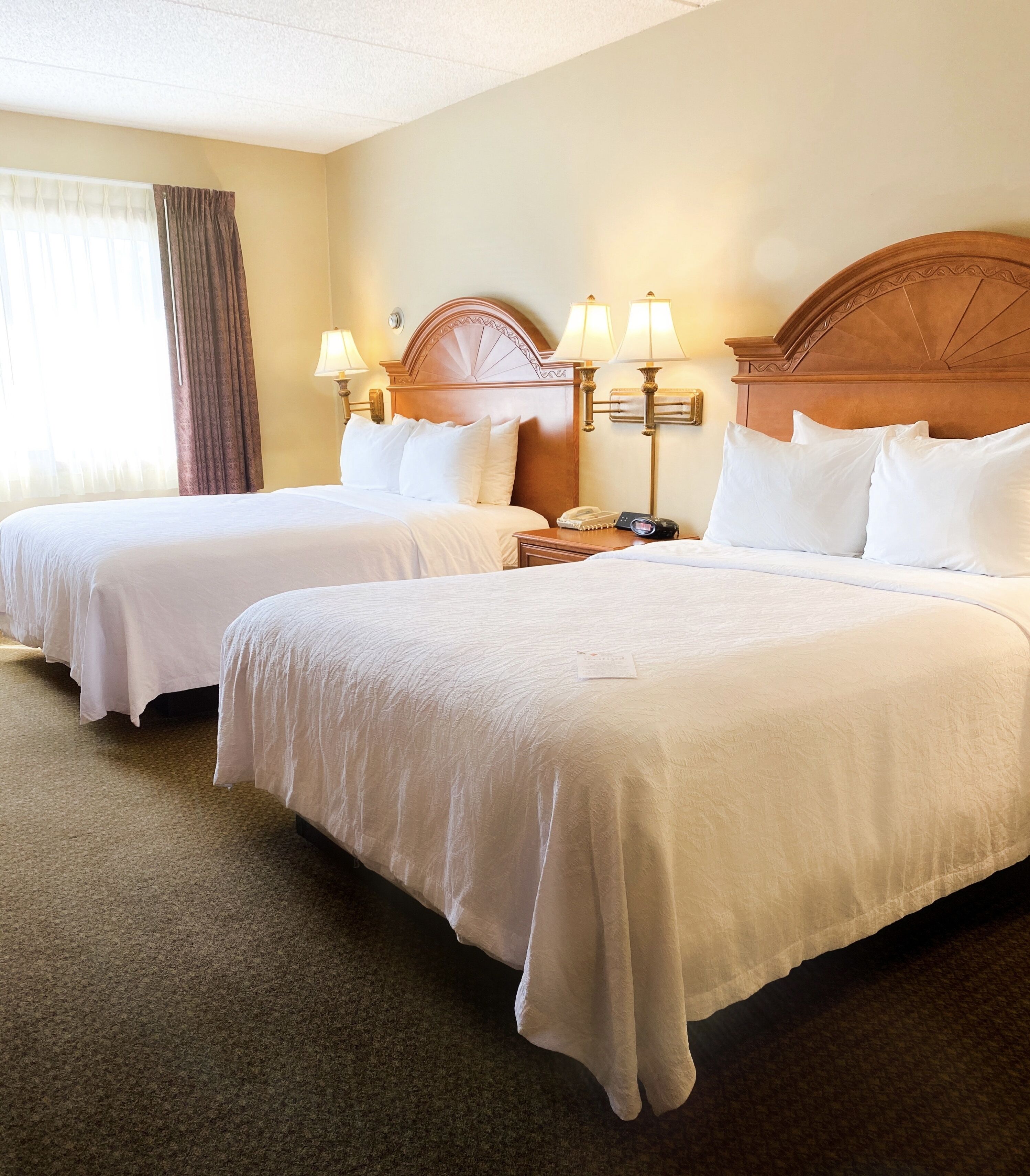 A hotel room with two single beds, a wooden headboard, bedside lamps, and a telephone on a nightstand.