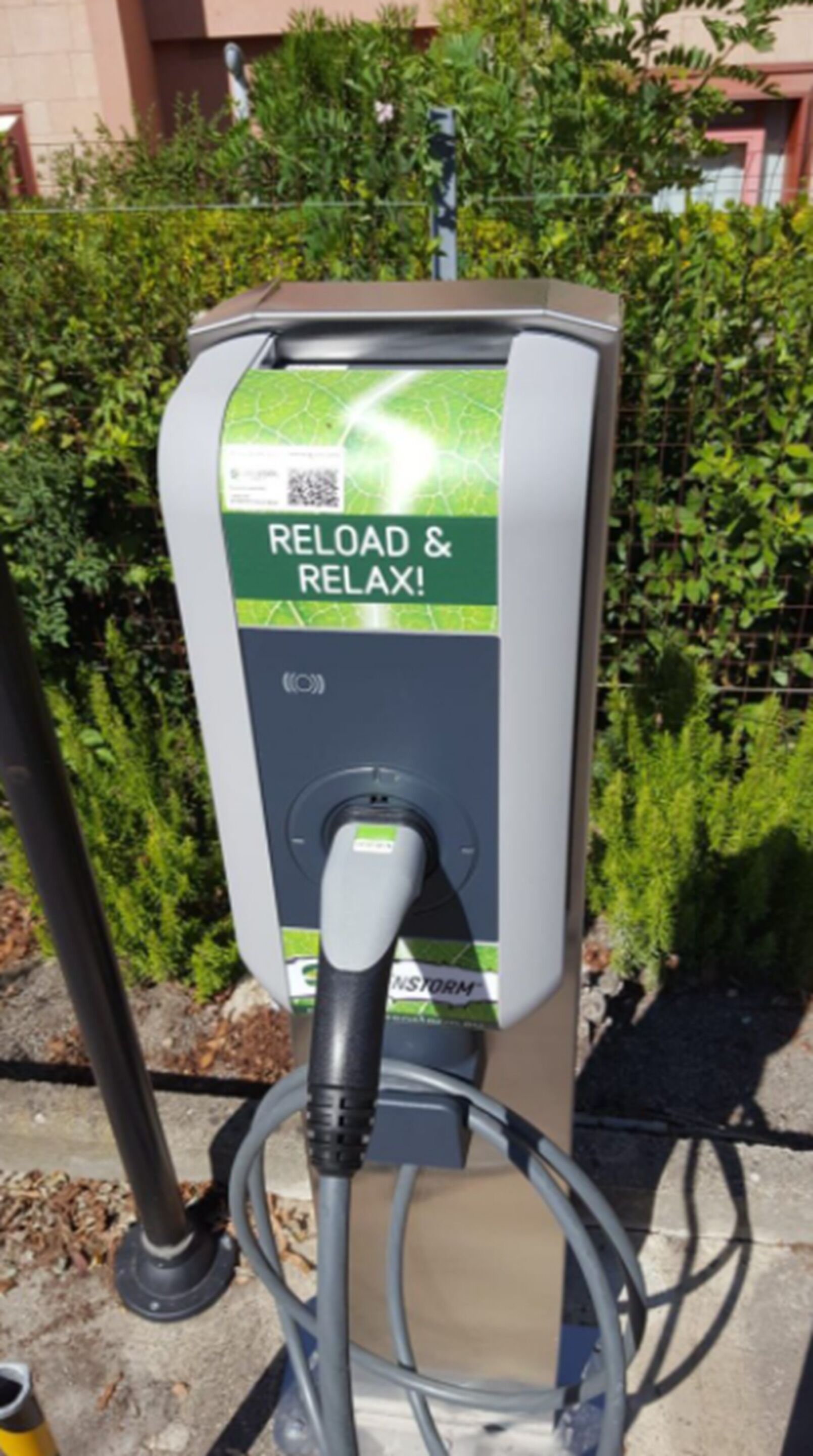 Una estación de carga para vehículos eléctricos con una etiqueta verde y blanca que dice 'RELOAD & RELAX!'