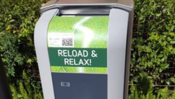 Una estación de carga para vehículos eléctricos con una etiqueta verde y blanca que dice 'RELOAD & RELAX!'