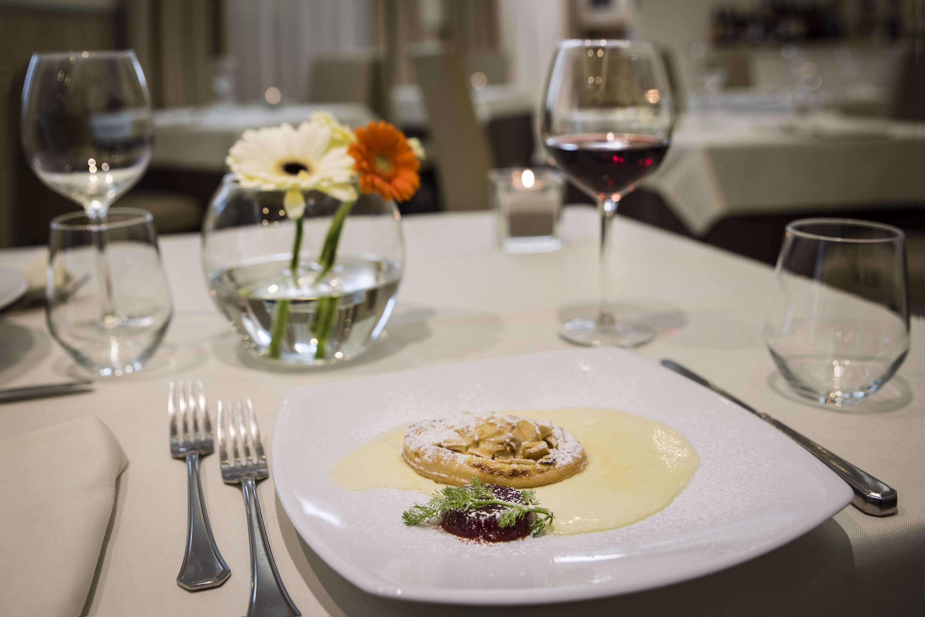 A dining table with a plate of food, a vase with flowers, and wine glasses.