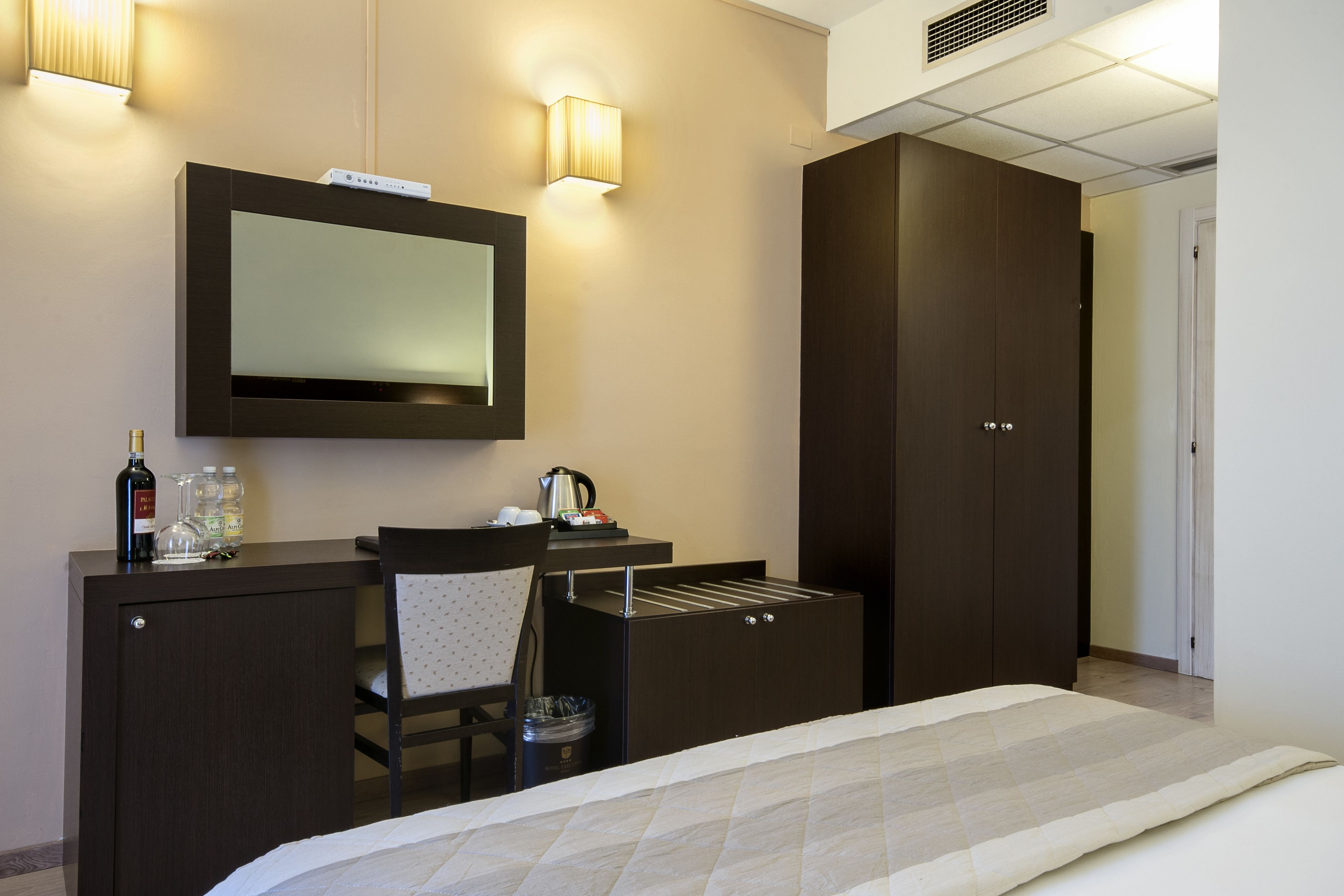 Een hotelkamer met een bed, een bureau met spiegel, een stoel, een kledingkast en een minibar.