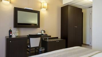 Een hotelkamer met een bed, een bureau met spiegel, een stoel, een kledingkast en een minibar.