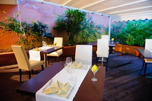 Enjoy dining al fresco under a covered roof, surrounded by lush greenery and comfortable seating.