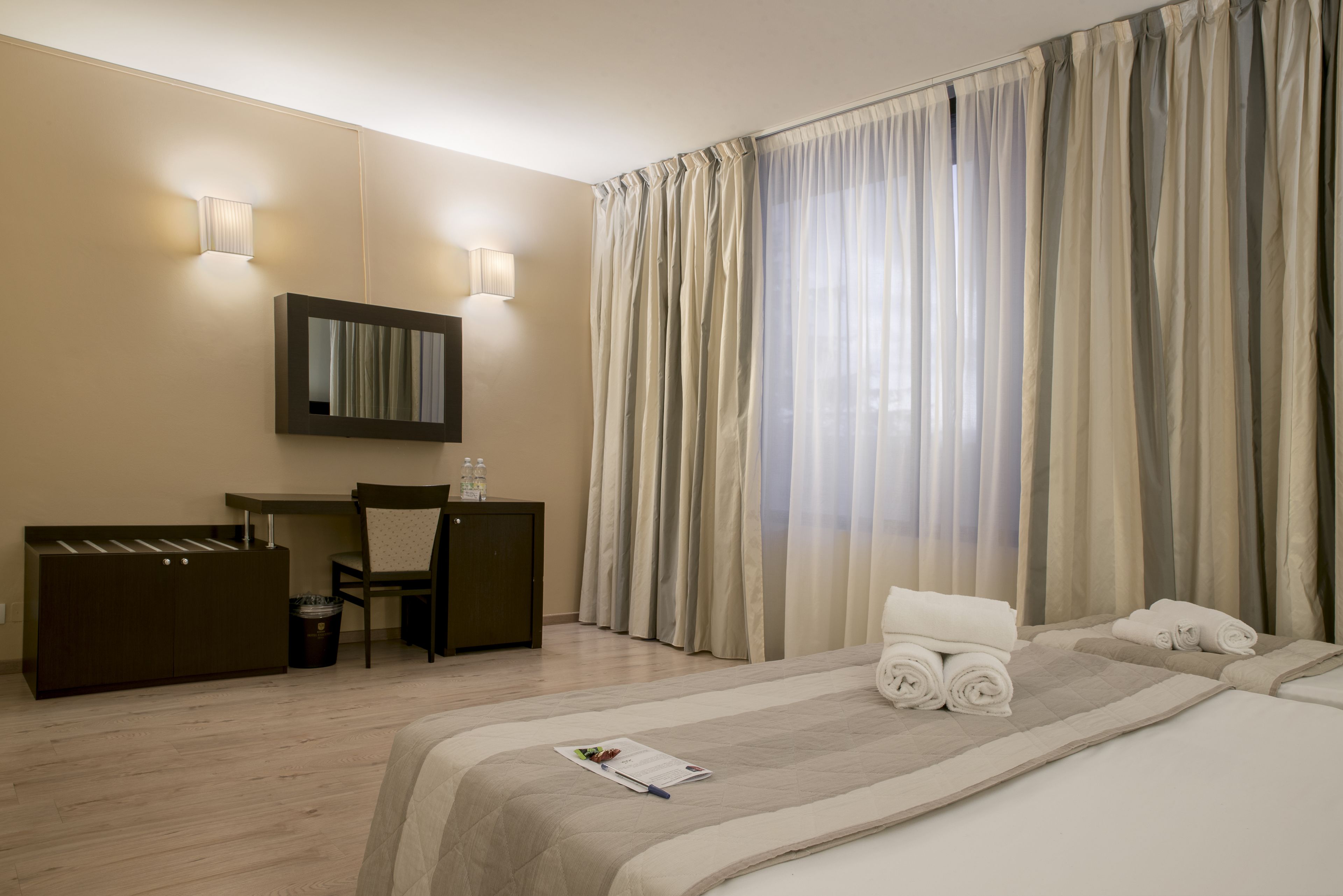 A hotel room with a bed, a desk, a chair, and a large window with curtains.