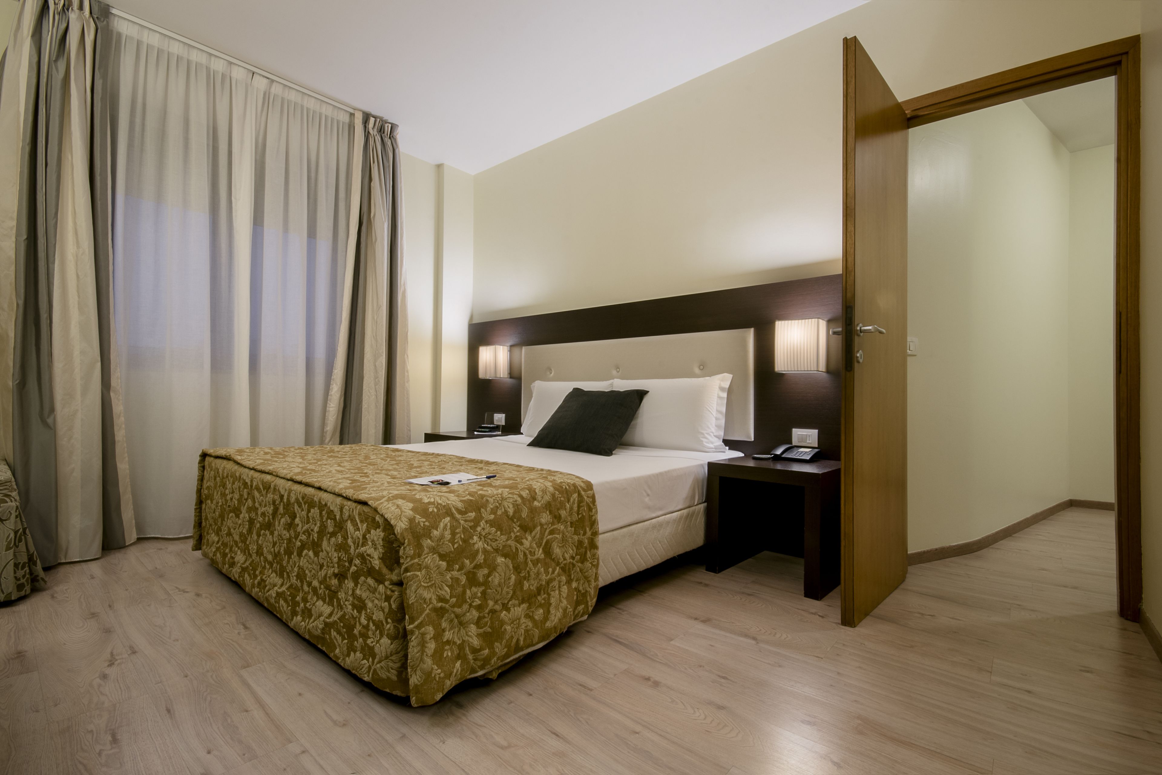 A hotel room with a bed, a nightstand, a lamp, and a door.
