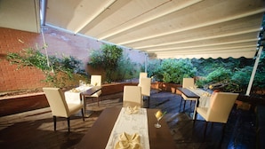 An outdoor dining area with tables and chairs, covered by a canopy, and surrounded by greenery. - Hotel Executive (Siena)